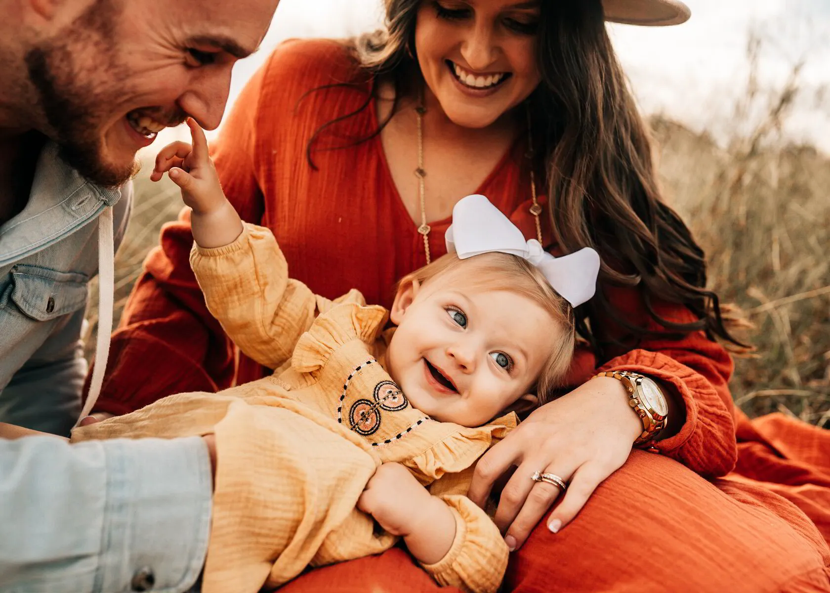A father, mother and toddler laughing together in tall autumn grass